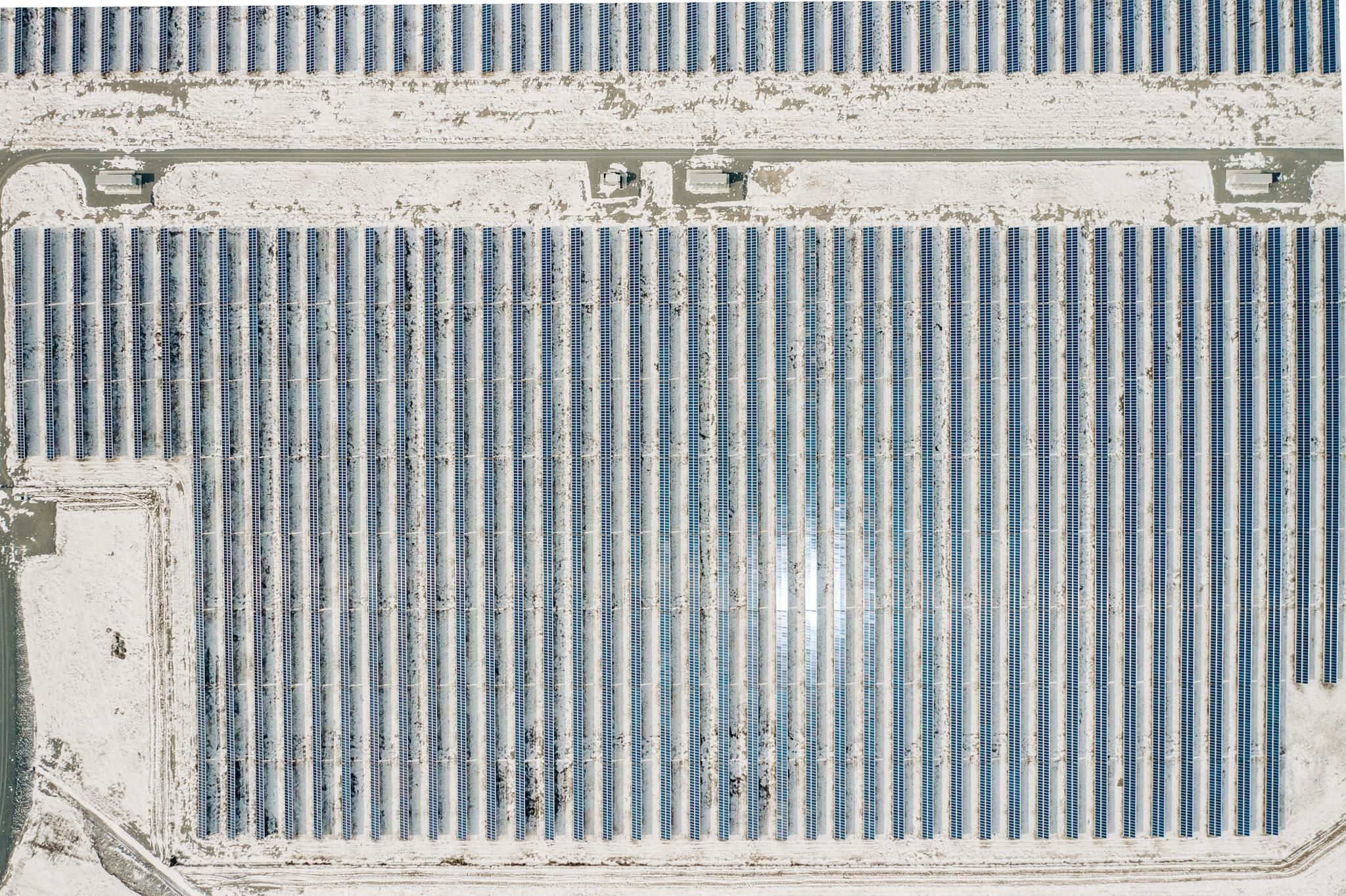 Drone shot of a solar farm amidst snow-covered terrain, showcasing renewable energy.